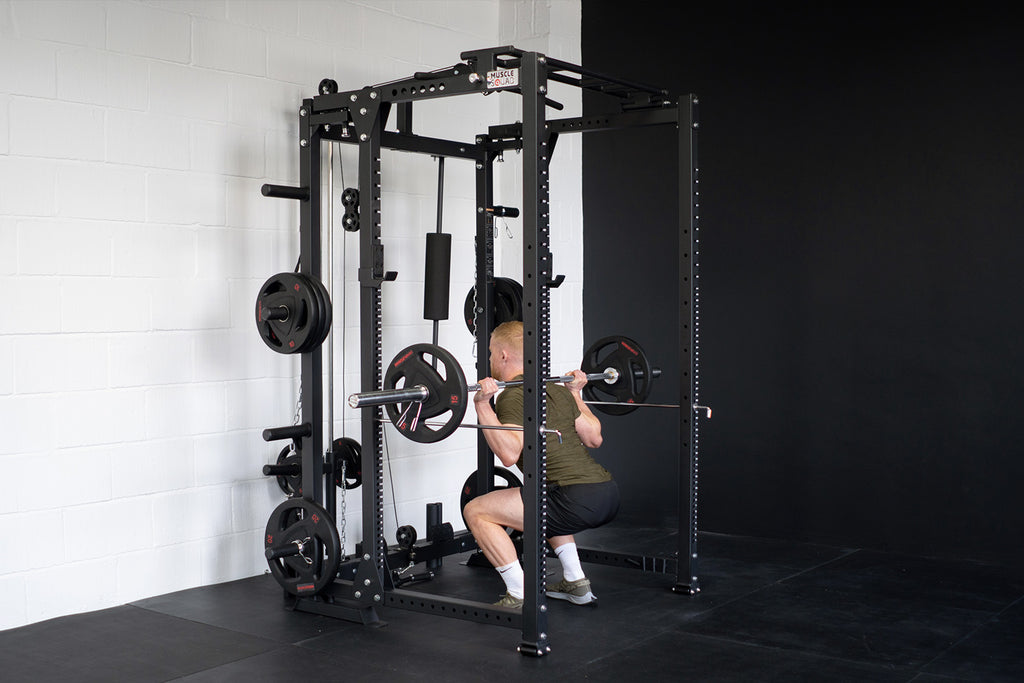 man doing a squat in a squat rack in a home gym setting